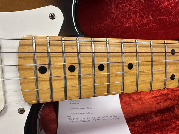 Close-up of maple guitar fretboard with black dot inlays and steel strings on white electric guitar body with red plush case background and handwritten notes underneath the neck