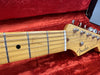 Close-up of Fender Stratocaster electric guitar headstock and maple fretboard with metal frets and strings inside red plush guitar case