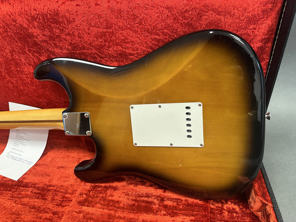 Rear view of sunburst electric guitar body with white backplate, showing neck joint and part of the maple neck, displayed on red velvet guitar case interior