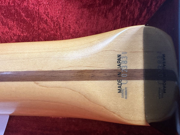 Close-up of guitar neck heel with "Made in Japan" and serial number 023831 stamped on natural wood finish against red fabric background