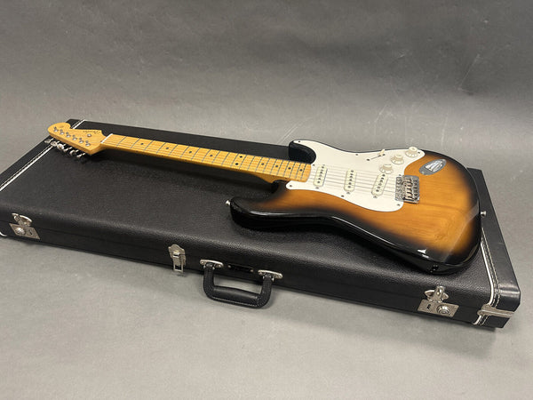 Fender Stratocaster electric guitar in sunburst finish lying on top of a black guitar hard case on a gray surface