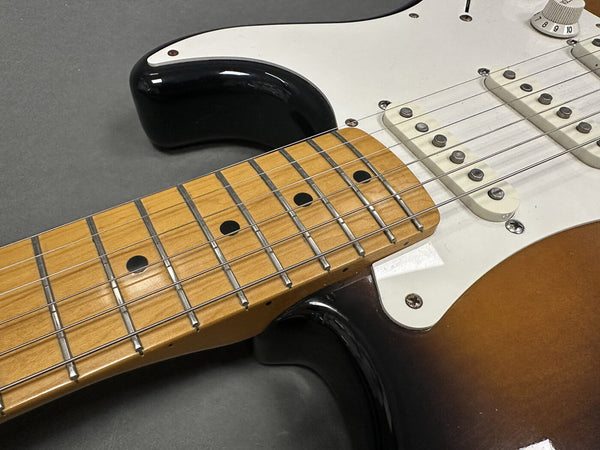 Close-up of sunburst electric guitar neck and fretboard with white pickguard and single coil pickups