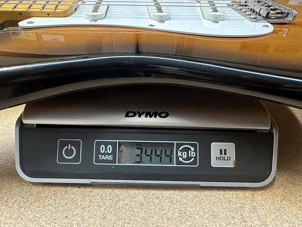 Close-up of electric guitar body on digital scale showing weight of 3.444 kilograms for Coffee House Guitars product listing.