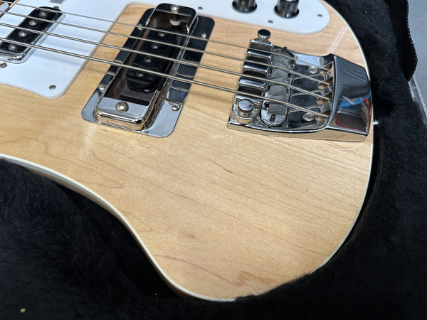 Close-up of natural wood finish electric bass guitar body with chrome bridge and pickup in black plush-lined case
