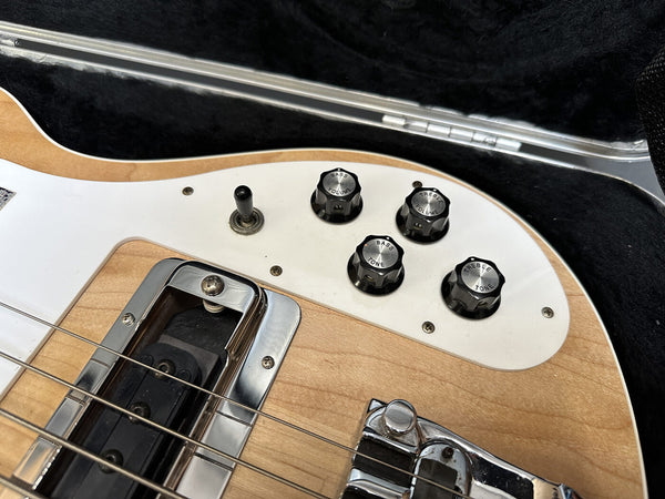 Close-up of electric bass guitar control knobs including bass volume, treble volume, bass tone, and treble tone on natural wood finish body in guitar case