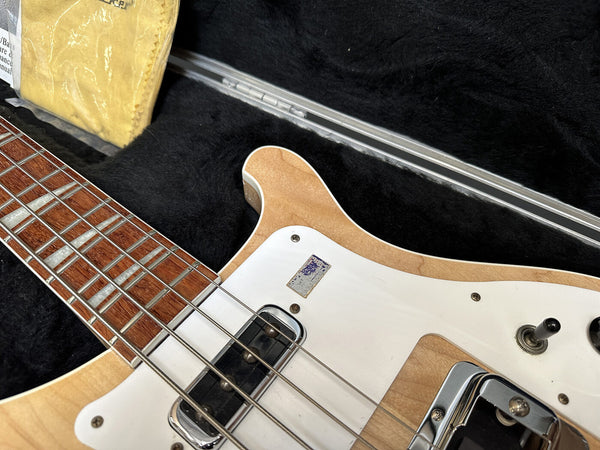 Close-up of natural finish electric guitar neck, strings, and white pickguard inside black plush guitar case with yellow cleaning cloth