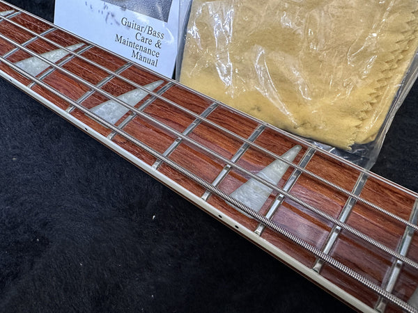 Close-up of bass guitar fretboard with pearl inlays and metal strings, guitar and bass care and maintenance manual, and yellow polishing cloth on black surface
