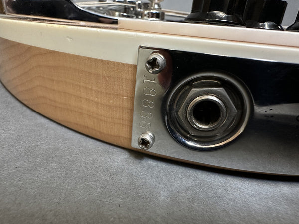 Close-up of guitar output jack plate with serial number 18888 on natural wood finish body edge.