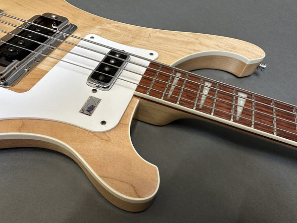 Close-up of natural finish electric bass guitar body and fretboard with white pickguard and trapezoid inlays on rosewood neck