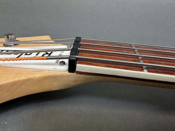 Close-up of electric bass guitar nut and strings on natural wood headstock with rosewood fretboard and white binding against gray background