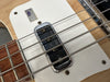 Close-up of electric bass guitar pickup and strings on white pickguard with natural wood body and rosewood fretboard.