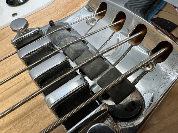 Close-up of electric bass guitar chrome bridge and pickups with natural wood body and metal strings at Coffee House Guitars product listing