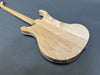 Back view of natural wood electric guitar body with maple neck and dual output jacks on gray surface