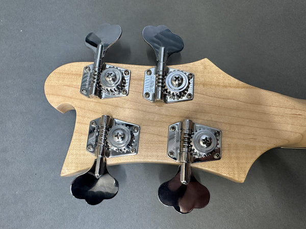 Close-up of four metal tuning pegs and gears on the back of a light wood bass guitar headstock against a dark background