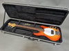 Sunburst electric bass guitar with white pickguard inside black hard guitar case with plush interior and extra electronic parts displayed