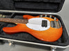 Vintage-style electric bass guitar with orange wood finish, white pickguard, four strings, and chrome hardware in a black hard case