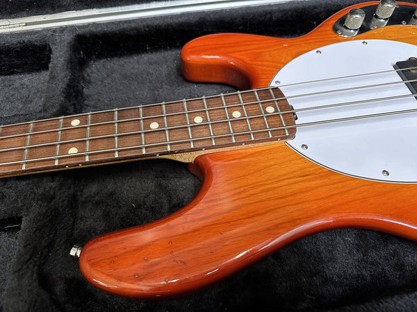 Close-up of orange electric bass guitar body and rosewood fretboard with white pickguard in black padded case