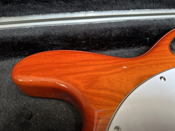 Close-up of the reddish-brown polished wood body of an electric guitar inside a black padded guitar case.