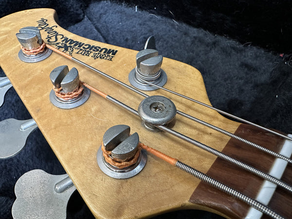 Closer view of vintage electric bass guitar headstock with metal tuning pegs and steel strings in black case interior