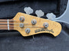 Close-up of Ernie Ball Music Man StingRay electric bass guitar headstock with tuning pegs and strings, natural wood finish.