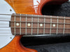 Close-up of electric bass guitar fretboard with metal frets, dot inlays, and strings on sunburst wood body with white pickguard in guitar case