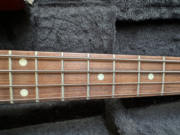 Close-up of bass guitar fretboard with dot inlays and metal strings on a dark padded background
