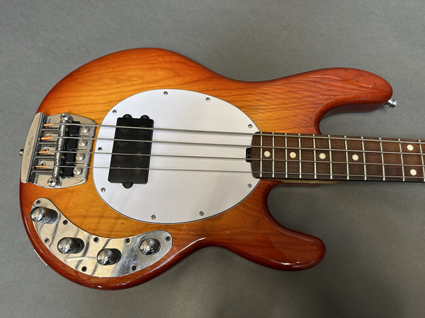 Electric bass guitar with sunburst finish, white pickguard, and chrome control knobs on gray background