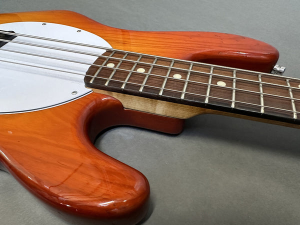 Close-up of electric bass guitar body and fretboard with sunburst finish and white pickguard on gray background