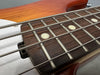 Close-up of bass guitar rosewood fingerboard with silver frets and round white inlays, showing thick metal bass strings on light wood neck and orange guitar body edge