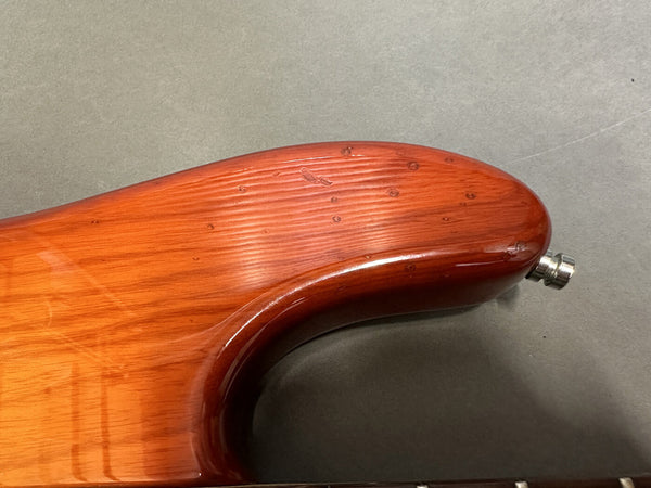 Close-up of brushed wood finish on the upper horn of an electric guitar body with a polished reddish-brown stain and metal strap button attached