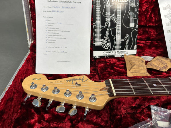 Fender Stratocaster guitar headstock with tuning pegs and rosewood fretboard resting in a red plush guitar case with Fender owner's manual and Coffee House Guitars pre-sales checklist.