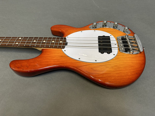 Vintage electric bass guitar with sunburst finish, white pickguard, four control knobs, and rosewood fretboard on gray background