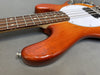 Close-up of orange electric bass guitar body and neck showing wood grain and white pickguard on gray background