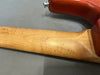 Close-up of the back of a guitar neck showing natural wood grain and the heel joint with a red guitar body on a gray surface