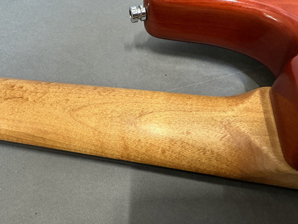 Close-up of the back of a guitar neck showing natural wood grain and the heel joint with a red guitar body on a gray surface