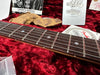 Close-up of a guitar fretboard with metal frets and dot inlays, surrounded by Fender owner's manual, warranty information, and silica gel packs on a red plush surface.