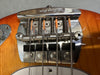 Close-up of vintage-style chrome guitar bridge with string saddles and springs on amber electric bass guitar body