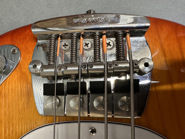 Close-up of vintage-style chrome guitar bridge with string saddles and springs on amber electric bass guitar body
