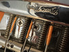Close-up of vintage Fender guitar bridge with wrapped guitar strings and engraved serial number 0970 on chrome metal plate