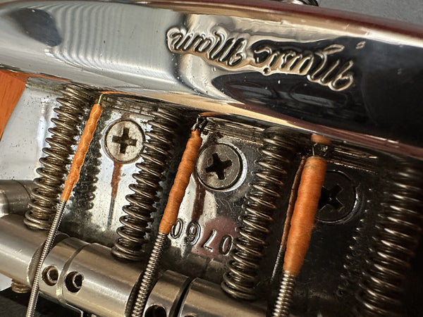 Close-up of vintage Fender guitar bridge with wrapped guitar strings and engraved serial number 0970 on chrome metal plate