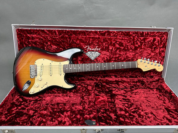 Fender Stratocaster electric guitar in sunburst finish with rosewood fretboard resting in red velvet-lined hardshell guitar case with Fender 60th anniversary logo inside lid.