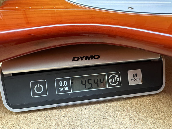 Close-up of a wooden guitar body resting on a Dymo digital scale showing the guitar weight as 4.544 kilograms.