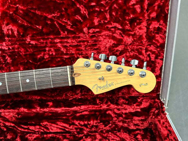 Fender Stratocaster guitar headstock close-up with six tuning pegs, made in USA, displayed on red plush guitar case lining