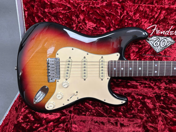 Fender Stratocaster electric guitar with sunburst finish, vintage white pickguard, three single-coil pickups, and rosewood fretboard resting on red plush guitar case lining with Fender 60 Diamond Anniversary embroidery.