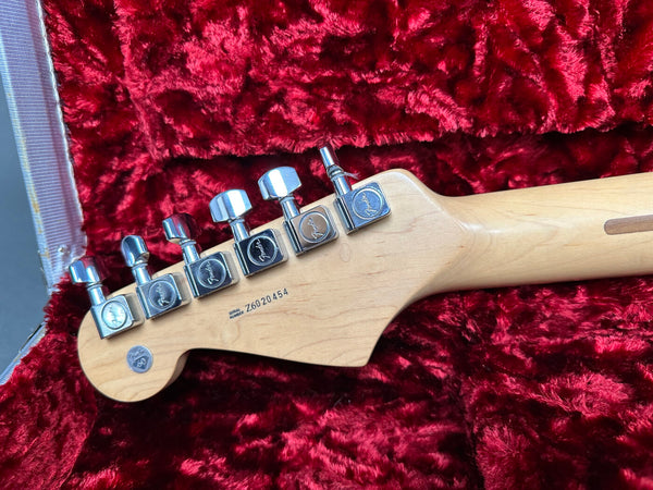 Close-up of Fender guitar headstock with chrome tuning pegs and serial number Z6020454 on a red plush guitar case lining.