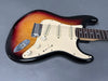 Electric guitar with sunburst finish, white pickguard, three single-coil pickups, and rosewood fretboard on gray background