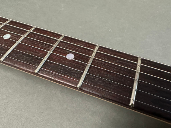 Close-up of dark wood guitar fretboard with metal frets and white dot inlays on acoustic guitar neck