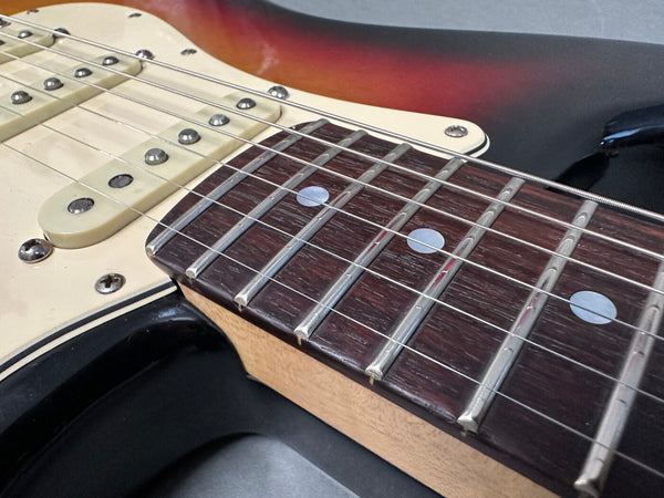 Close-up of electric guitar fretboard and strings on a sunburst body with cream pickguard and single coil pickups