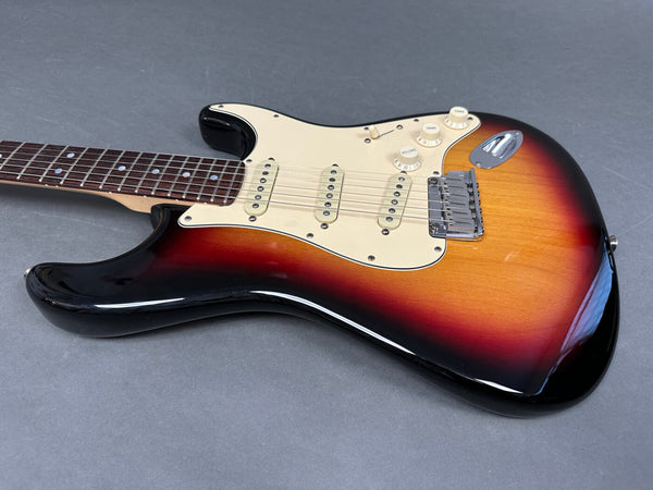 Sunburst electric guitar with rosewood fretboard and white pickguard, three single-coil pickups, volume and tone control knobs on gray background