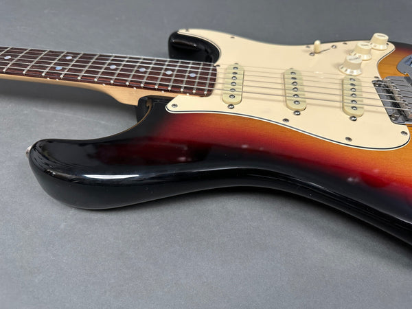 Close-up of sunburst electric guitar body and rosewood fingerboard with white pickguard and three single-coil pickups on gray background